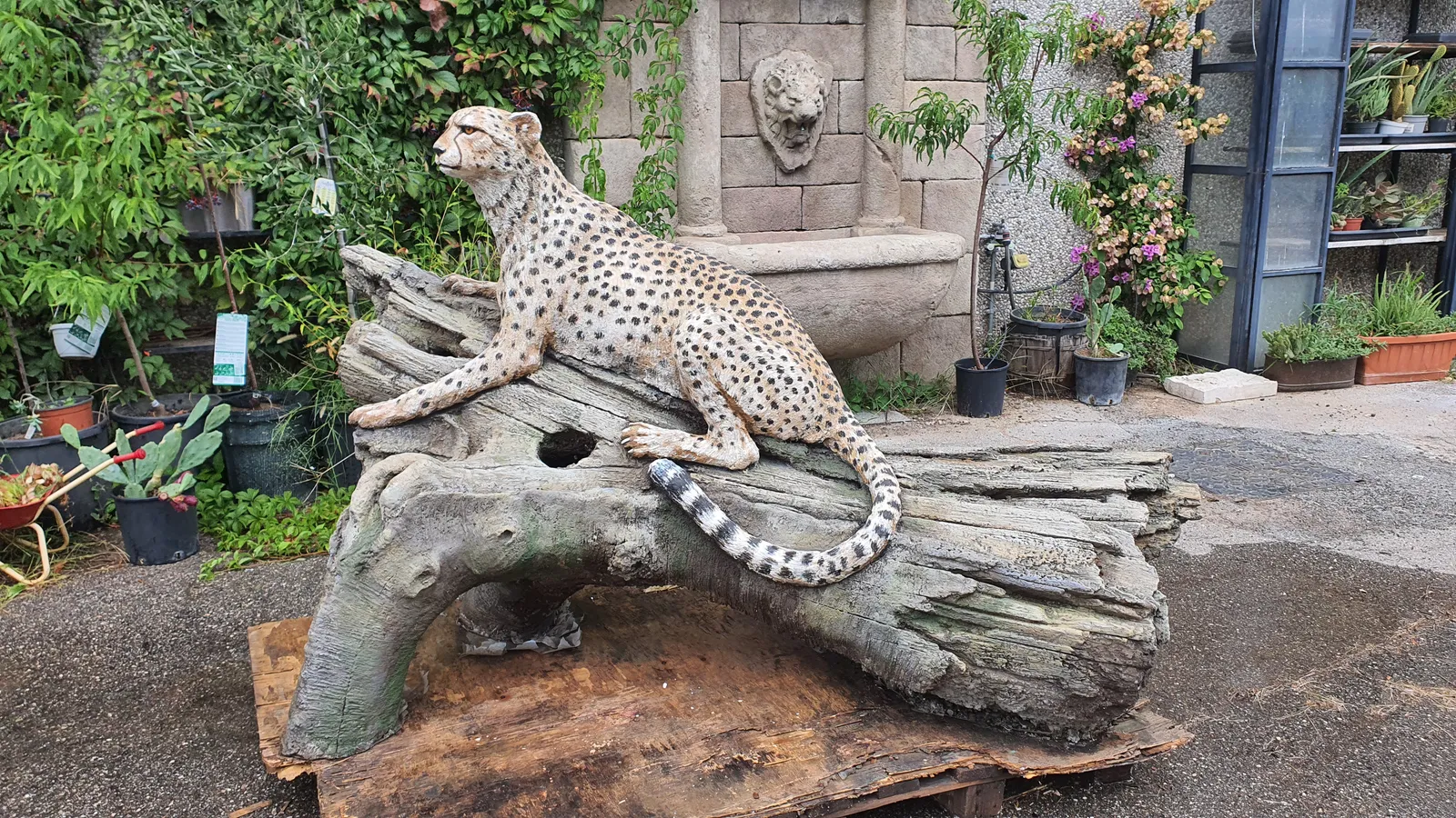 Side view of a hand-shaped concrete cheetah with painted markings resting on a modeled artificial trunk.