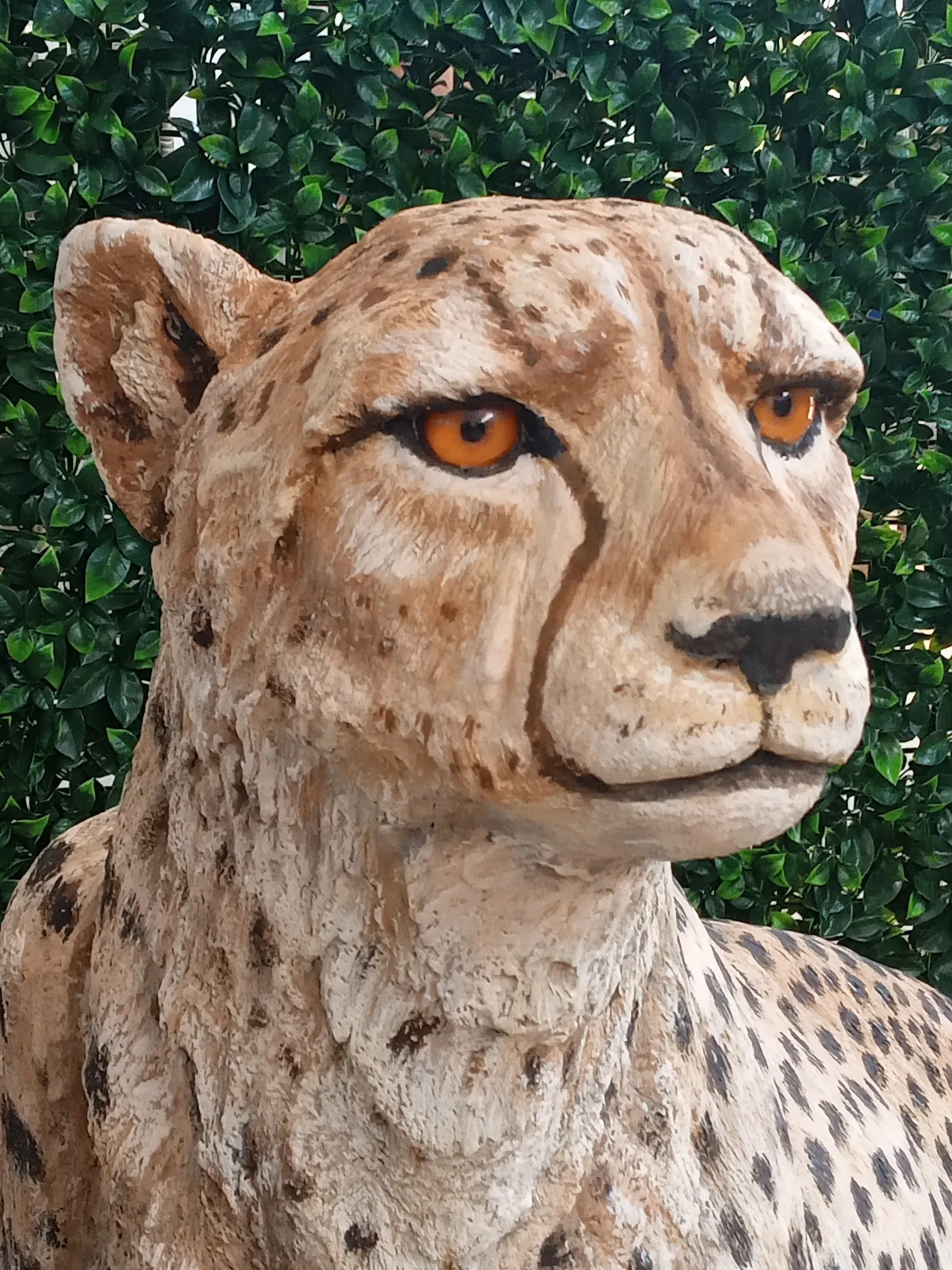Close view of the concrete cheetah’s modeled head with painted facial markings and amber-colored eyes.