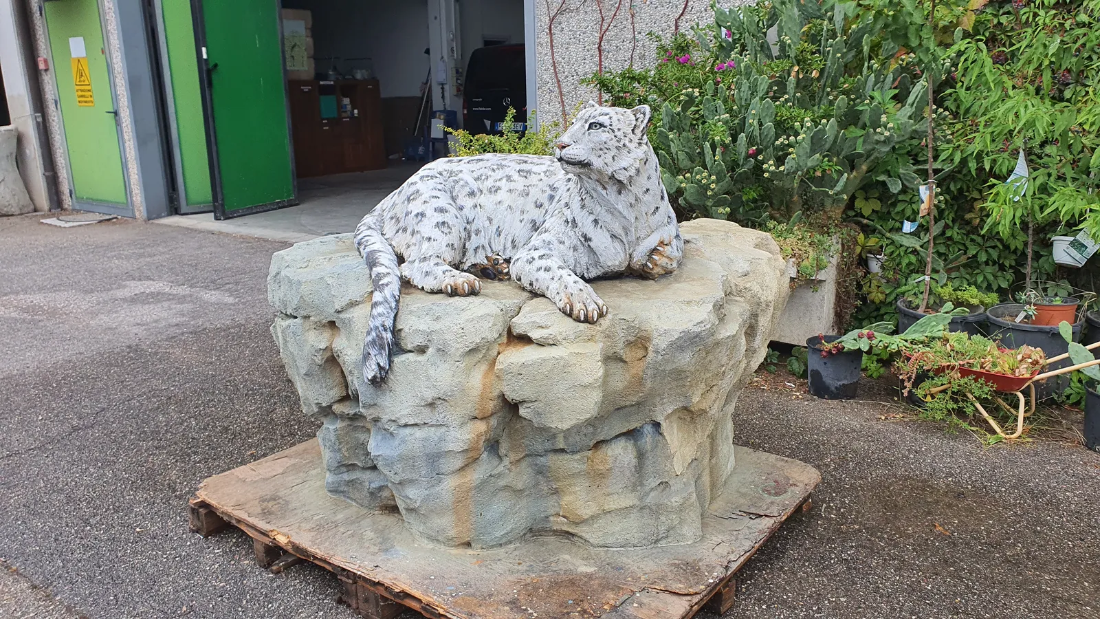 Hand-shaped concrete snow leopard reclines on an artificial rock with its long tail hanging over the front edge.
