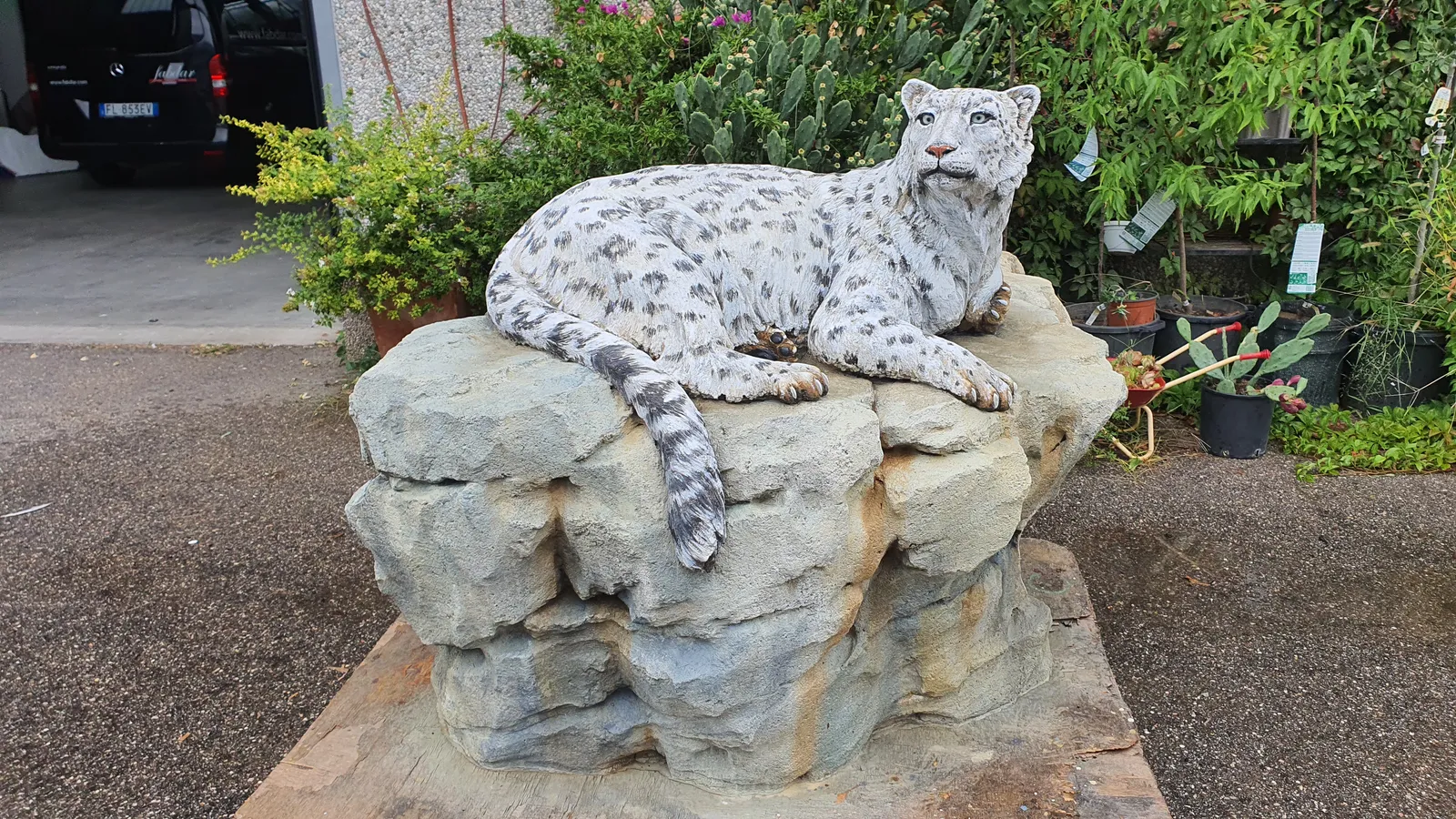 Front three-quarter view of the concrete snow leopard showing modeled fur, extended forepaws and a hanging tail.